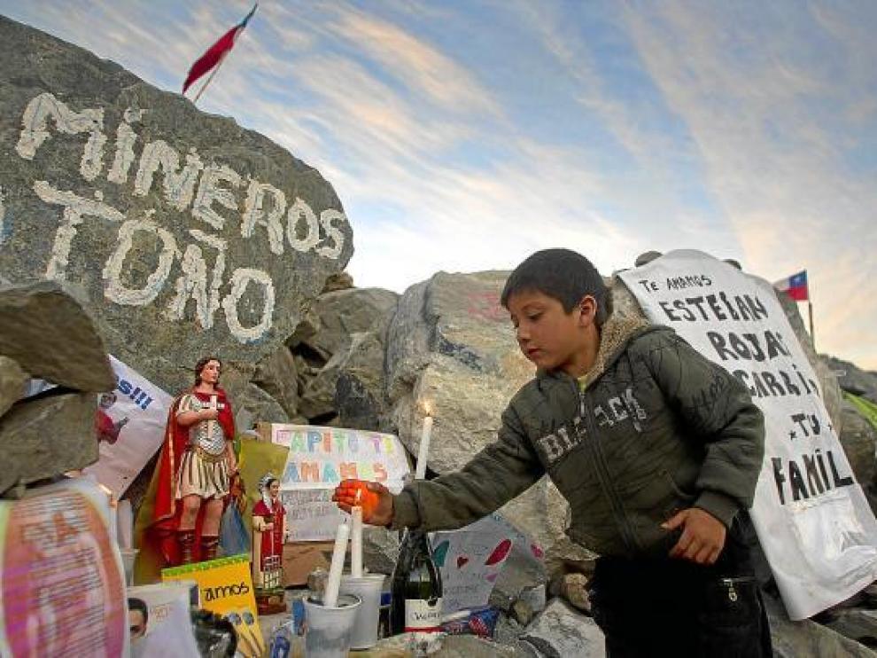 Un niño enciende una vela en un altar del campamento de la mina San José (Chile), ayer.