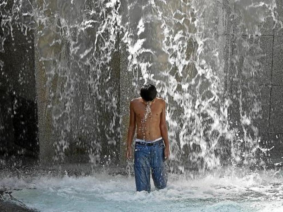 Un chaval se refresca en la fuente de la Hispanidad de la plaza del Pilar de Zaragoza.