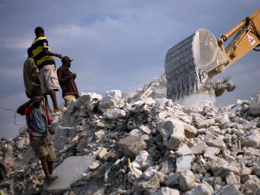 Unos haitianos observan una grúa desde una montaña de escombros, un año después de la tragedia