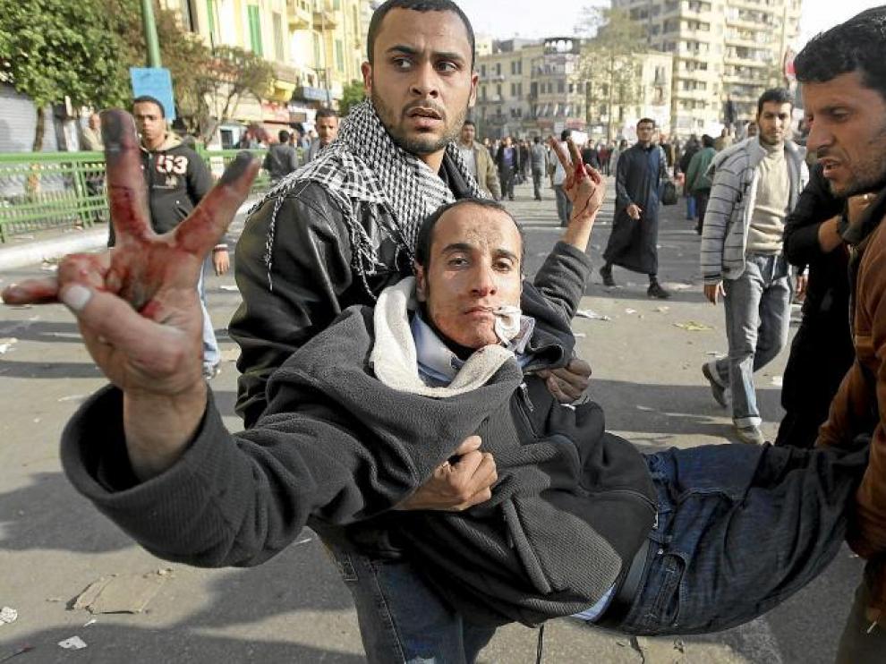 Dos egipcios trasladan a un herido durante los enfrentamientos en la plaza de Tahrir, ayer en El Cairo.