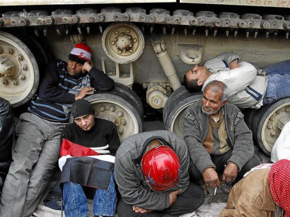 Varios manifestantes se protegen de la lluvia junto a un tanque junto a la plaza de Tahrir.