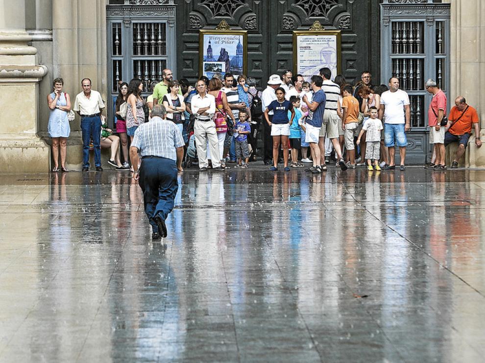 Paseantes y turistas se refugian de una tormenta en la entrada a la basílica del Pilar.