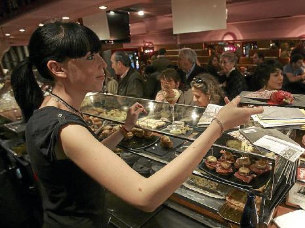 Una camarera sirve una tapa ante un público muy numeroso