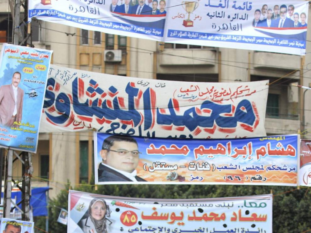 Dos mujeres y un niño pasean ante carteles electorales en El Cairo