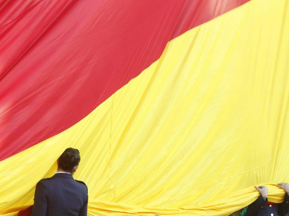 Dos militares despliegan la bandera nacional durante el acto solemne de izado de la enseña en Madrid