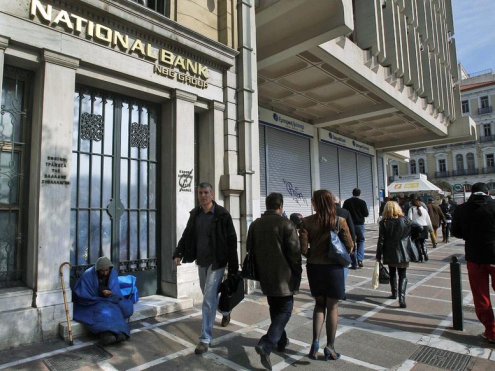 Varias personas caminan junto a una oficina del Banco Nacional de Grecia