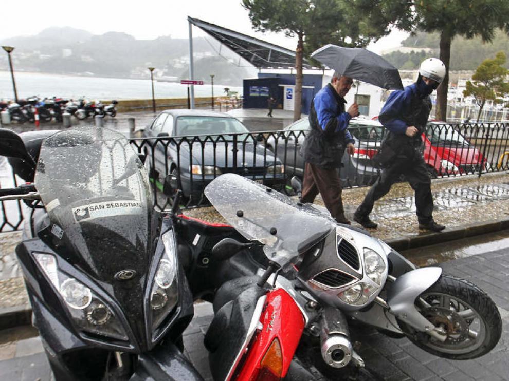 Dos conductores observan unos vehiculos derribados por el temporal en San Sebastián