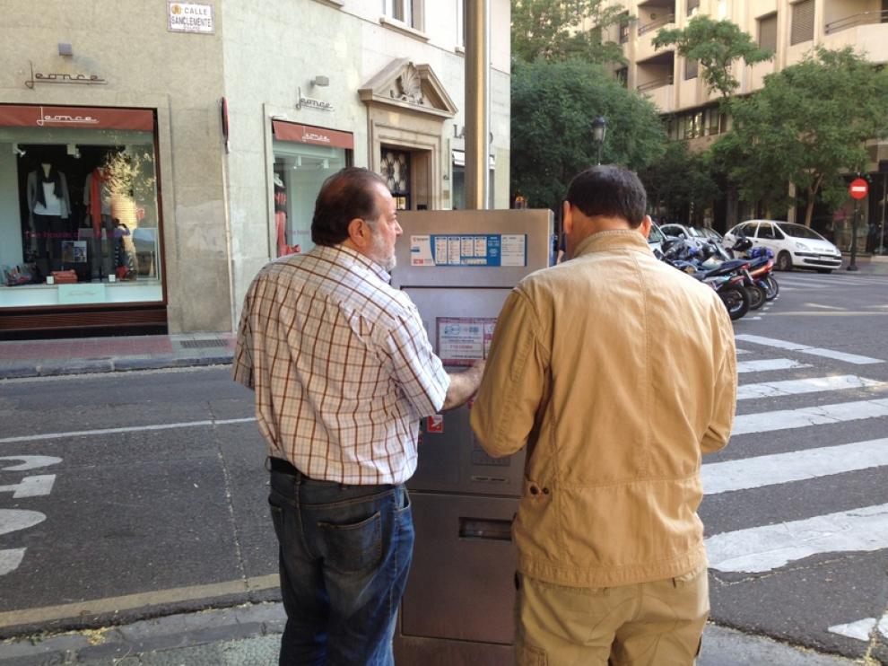 Dos personas intentando sacar el ticket del parquímetro