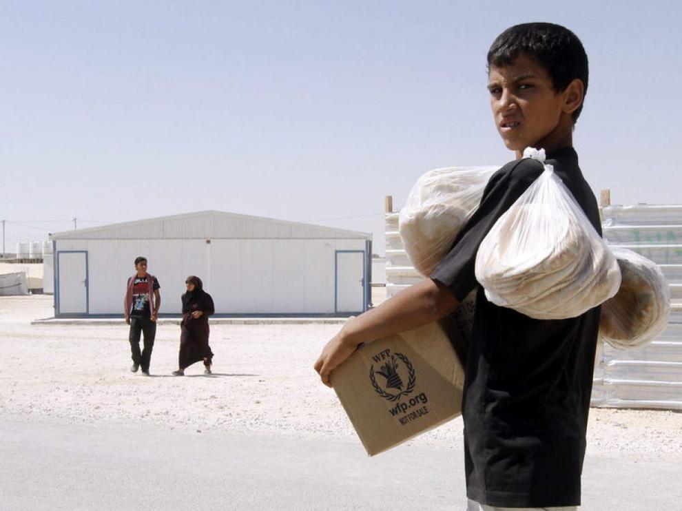 Un refugiado sirio carga con provisiones en un campo de refugiados de Zattari