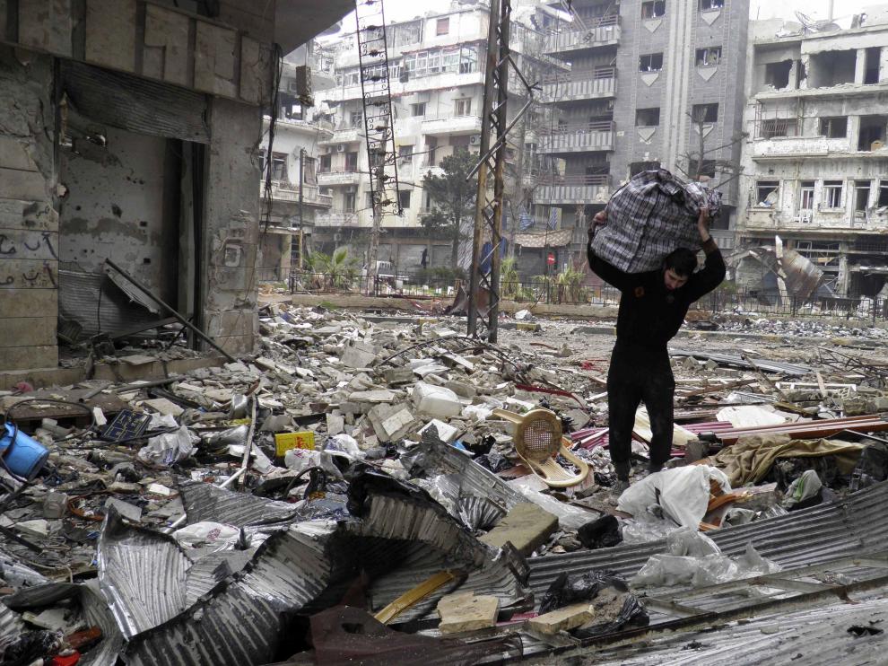 Un hombre carga con una bolsa entre las ruinas de Homs
