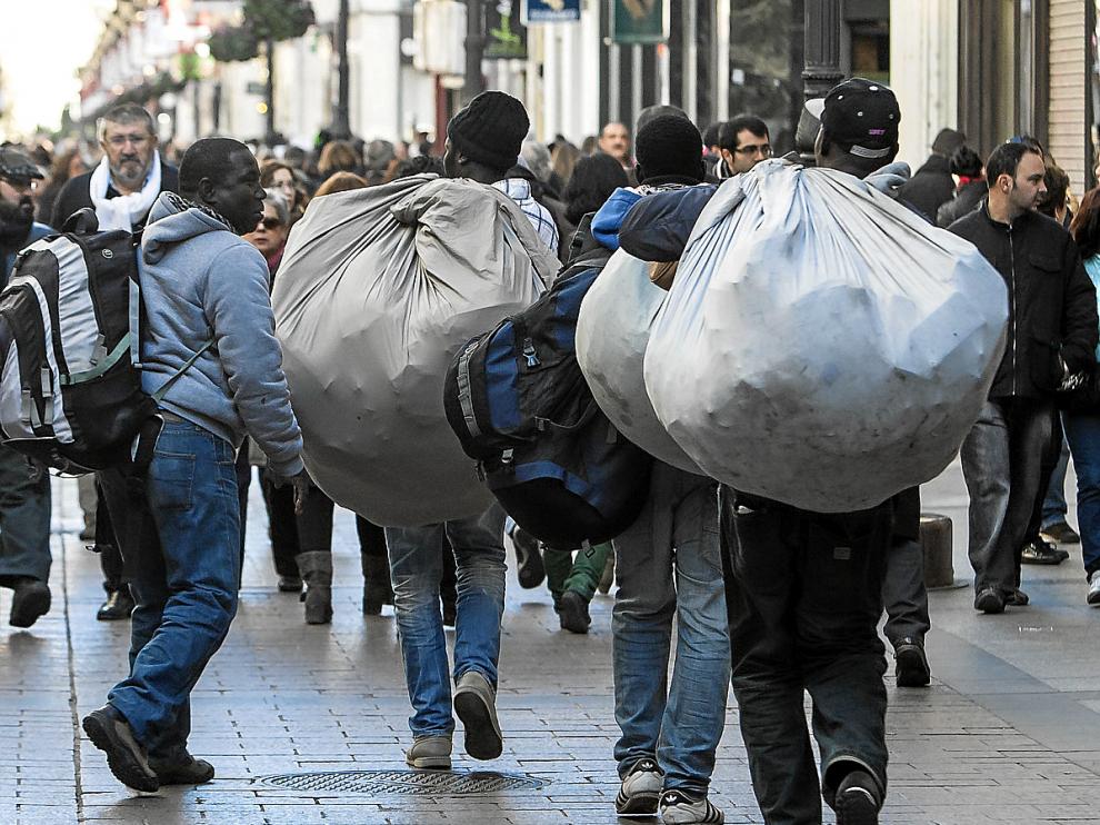 Cuatro manteros transportan su mercancía por la calle de Alfonso I de Zaragoza.