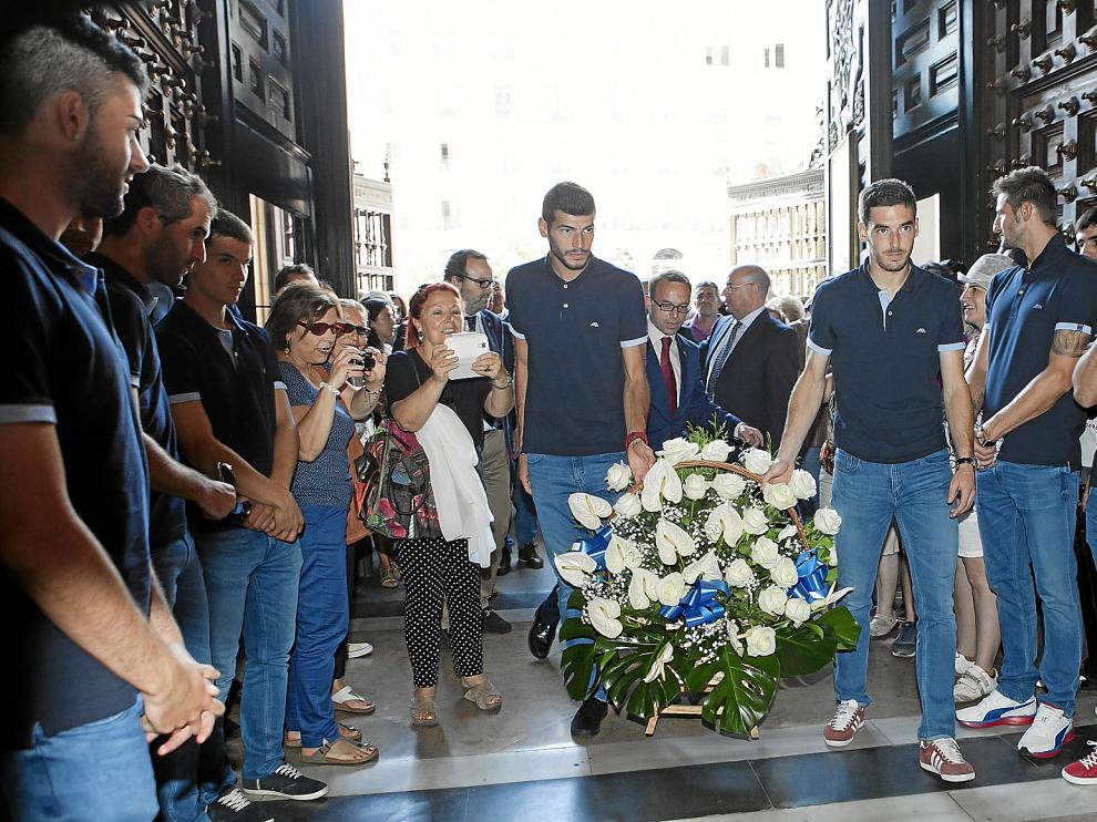 Álamo y Alcolea hacen su entrada a la Basílica con la cesta floral, escoltados por el resto de la plantilla y por el presidente del club, Christian Lapetra.