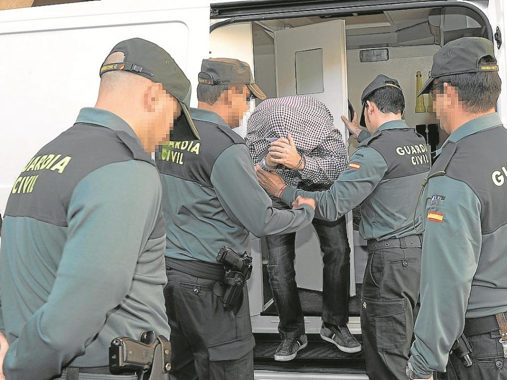 Uno de los detenidos se cubre la cabeza con su ropa al bajar del furgón policial.