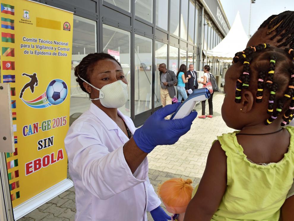 Una trabajadora sanitaria comprueba la temperatura de una niña pequeña en el aeropuerto de Bata (Guinea).