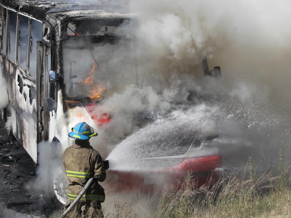 Un bombero apaga uno de los autobuses incendiados en los disturbios de Jalisco.