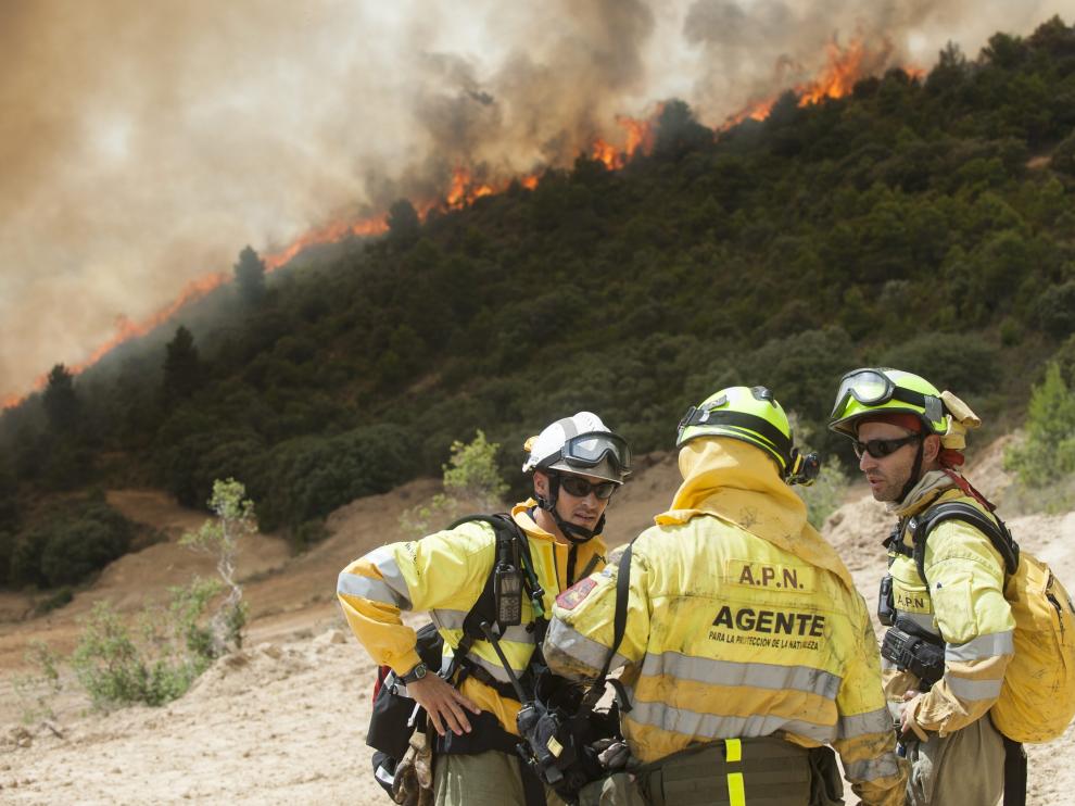 Tres miembros del operativo, con el incencio al fondo