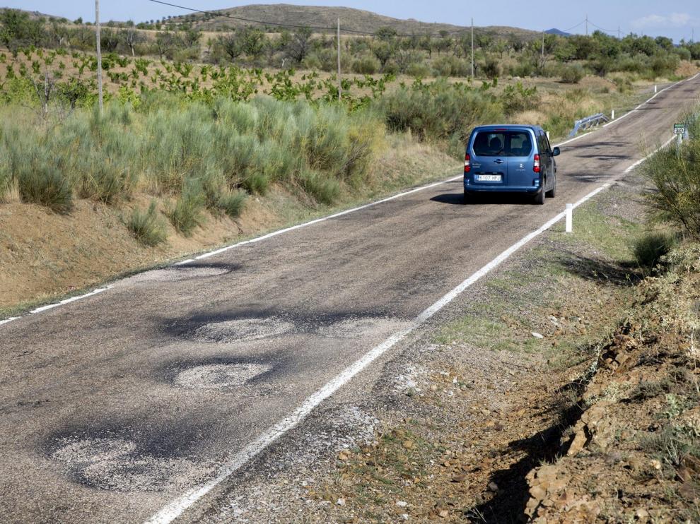 Un vehículo circula por la A-1503. La imagen muestra la calzada llena de baches recién parcheados.