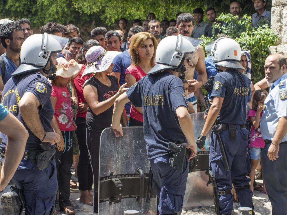 Varios policías vigilan a los inmigrantes que esperan en fila delante de una comisaría.