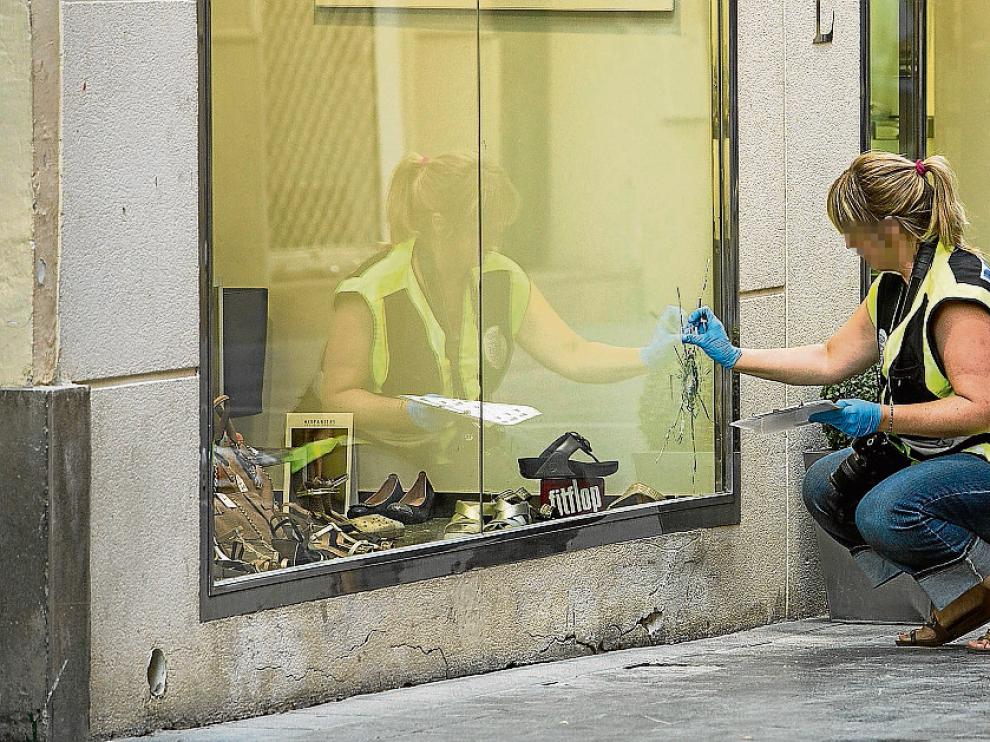 Una agente recoge muestras de los impactos de bala en un escaparate de la calle de Candalija.