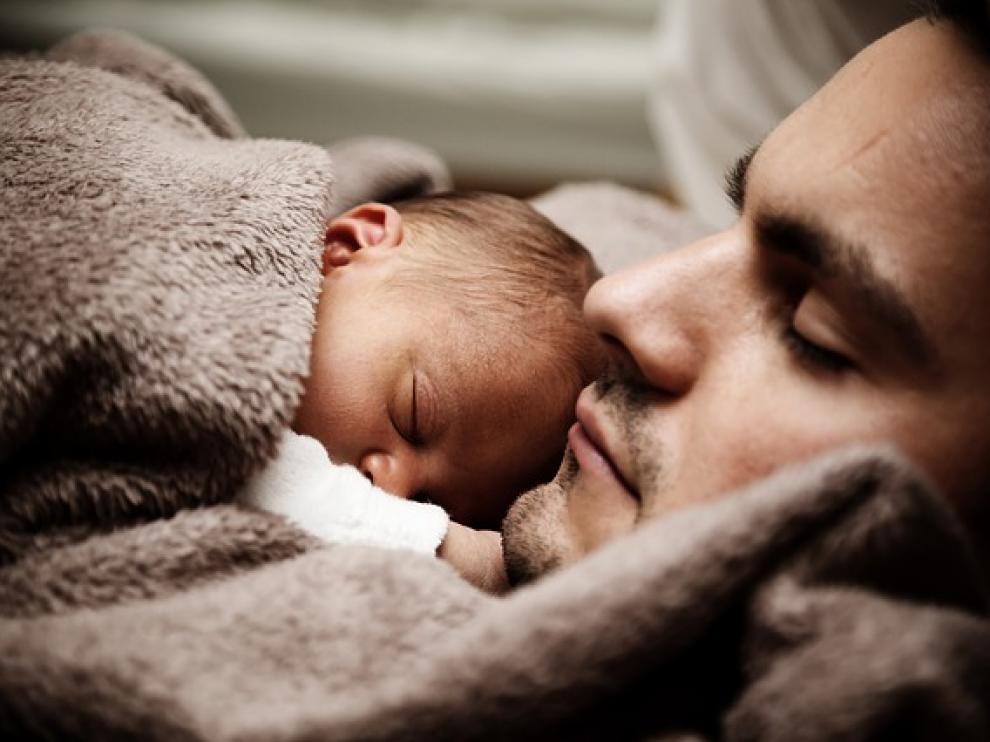 Un padre duerme junto a su bebé.