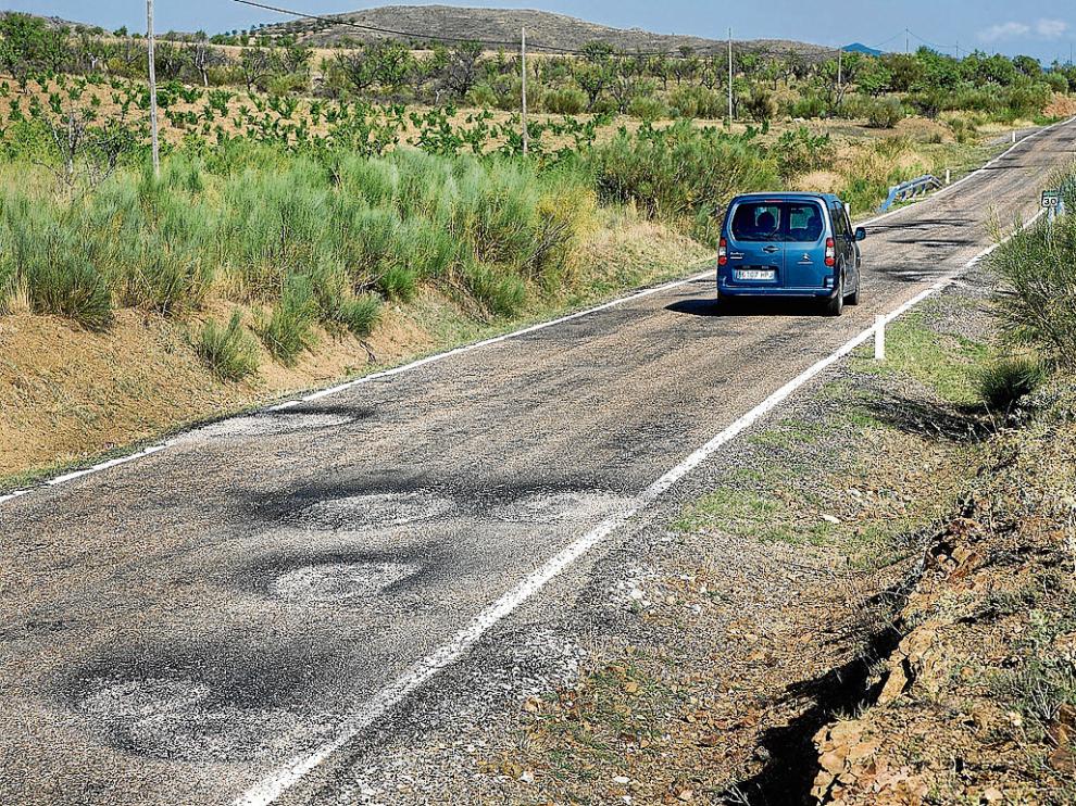 Un vehículo circula por la A-1503. La imagen muestra la calzada llena de baches recién parcheados.