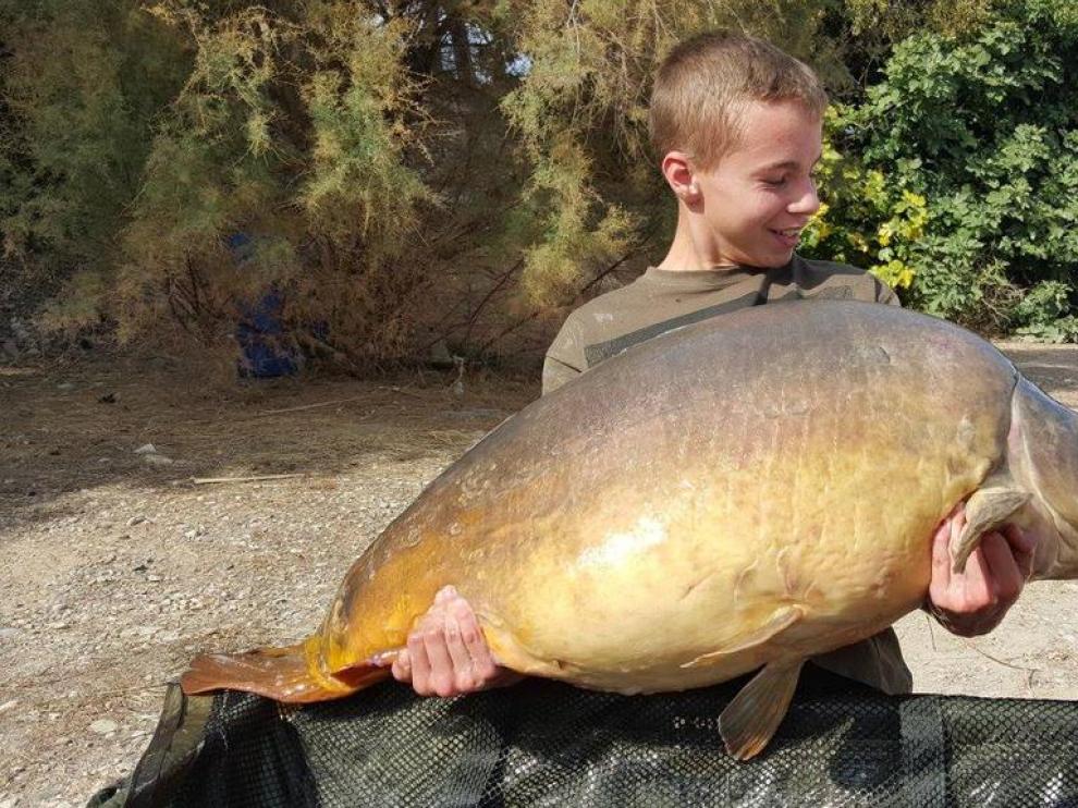 El joven pescador posa con la carpa capturada.