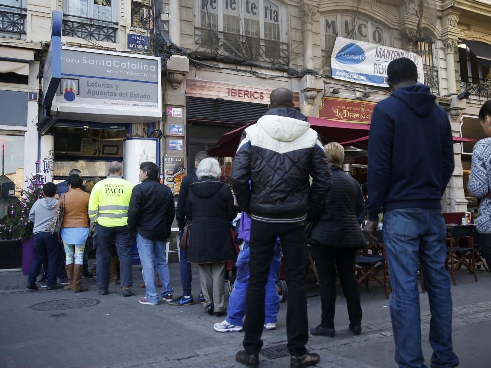 Un grupo de pesonas guarda cola ante una administración de lotería del centro de la ciudad para adquirir los décimos para el sorteo de la Lotería de Navidad