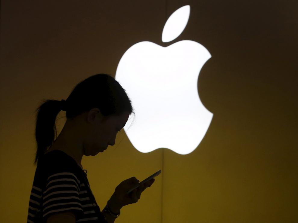 Una mujer mira la pantalla de su móvil frente a un logo de Apple