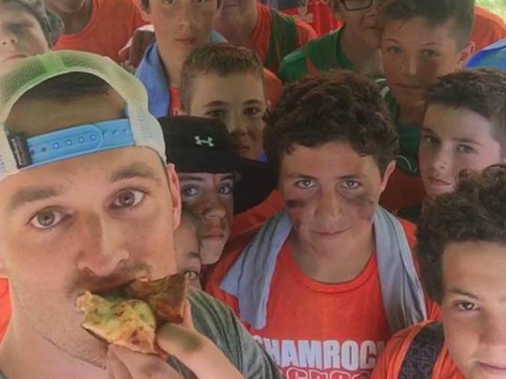 Kyle Feeney tomando una porción de pizza, rodeado de jóvenes.