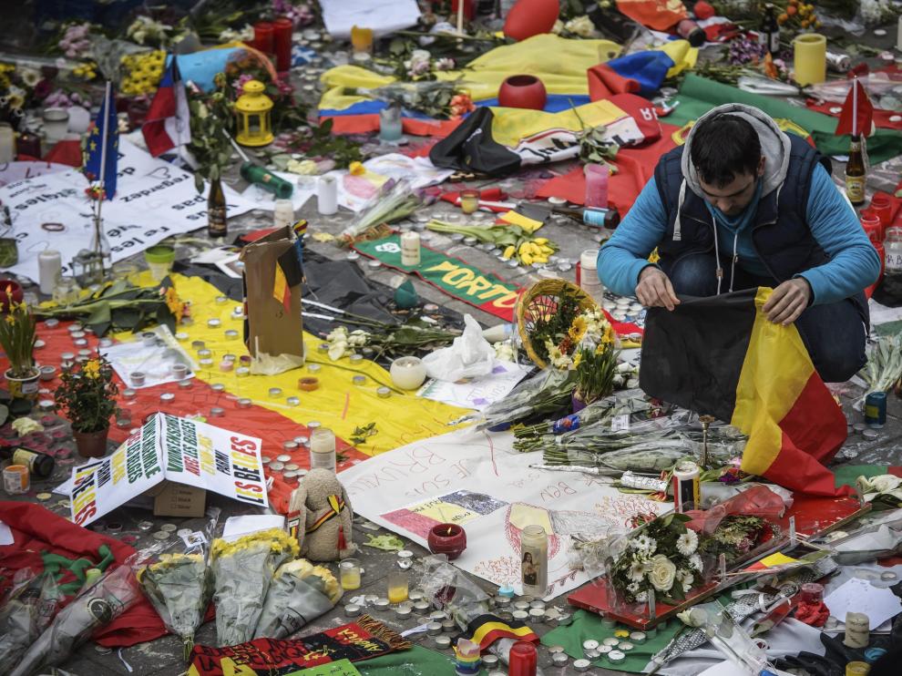 Un joven deposita una bandera de Bélgica junto a mensajes, flores y velas en homenaje a las víctimas.