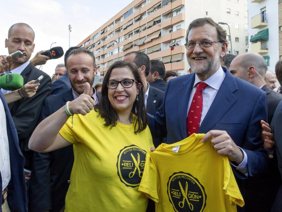 El presidente del Gobierno en funciones y candidato del PP a la reelección, Mariano Rajoy (d), con una simpatizante que lleva una camiseta de 'No a los recortes Religión'