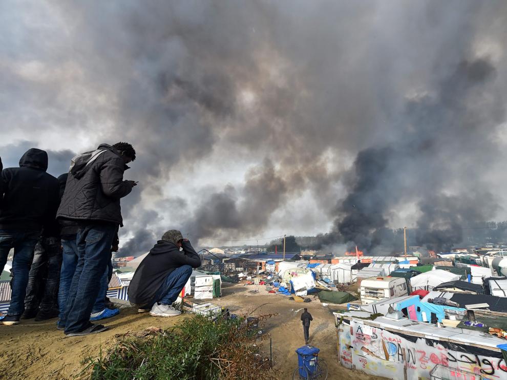 Varios inmigrantes ven parte del campamento ardiendo.