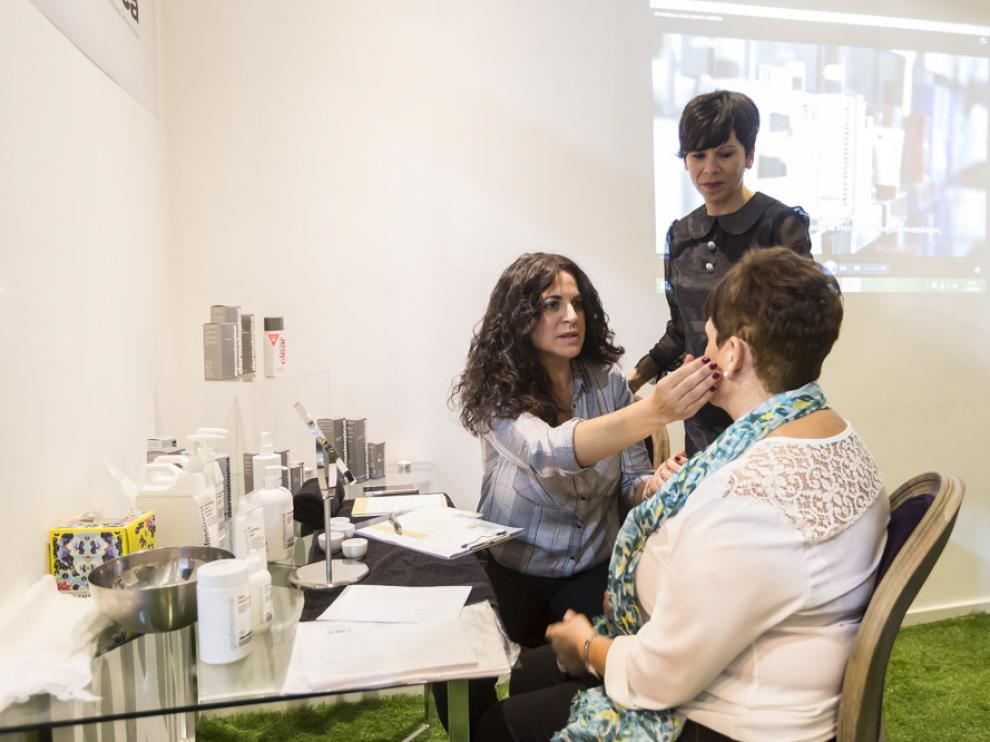 Eva Porroche, de pie, y Mari Carmen Valero, sentada, analizando por zonas la piel de una clienta mediante la técnica del ´face mapping`.