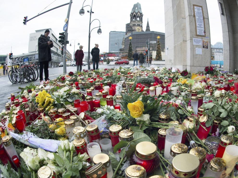 Varias personas pasan junto a las velas y las flores en la plaza Breitscheidplatz.