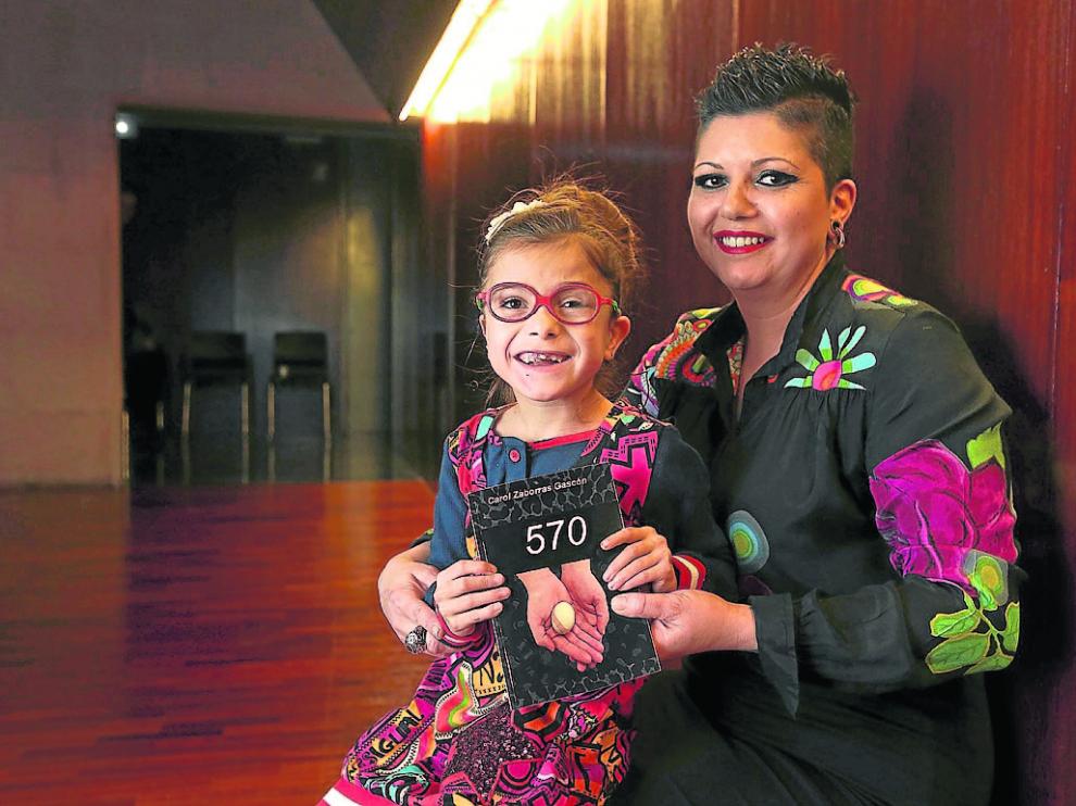 Carol Zaborras, con su hija Libe en brazos, que enseña el libro '570' donde narra su experiencia.