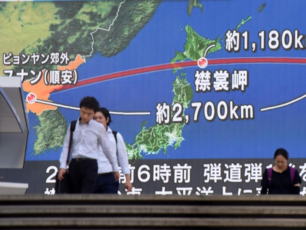 Varios viandantes en Tokio pasan delante de una pantalla que muestra la trayectoria del misil.