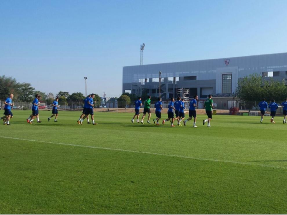 Los jugadores del Real Zaragoza, al mediodía de este sábado, entrenándose en el campo anejo al Viejo Nervión en la Ciudad Deportiva del Sevilla FC, donde jugarán por la noche frente al Sevilla Atlético. Al fondo se aprecia la fachada de la nueva tribuna del recinto recién estrenado en agosto.