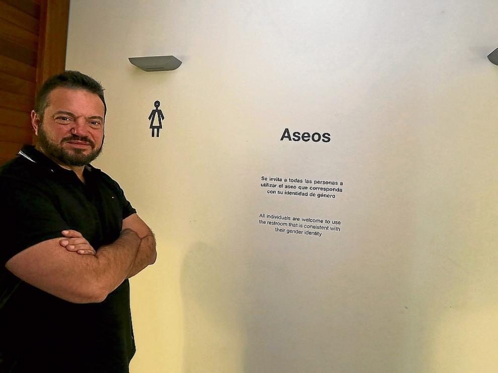 Juan Guardiola junto al cartel que invita a "utilizar el aseo que corresponda con su identidad de género".