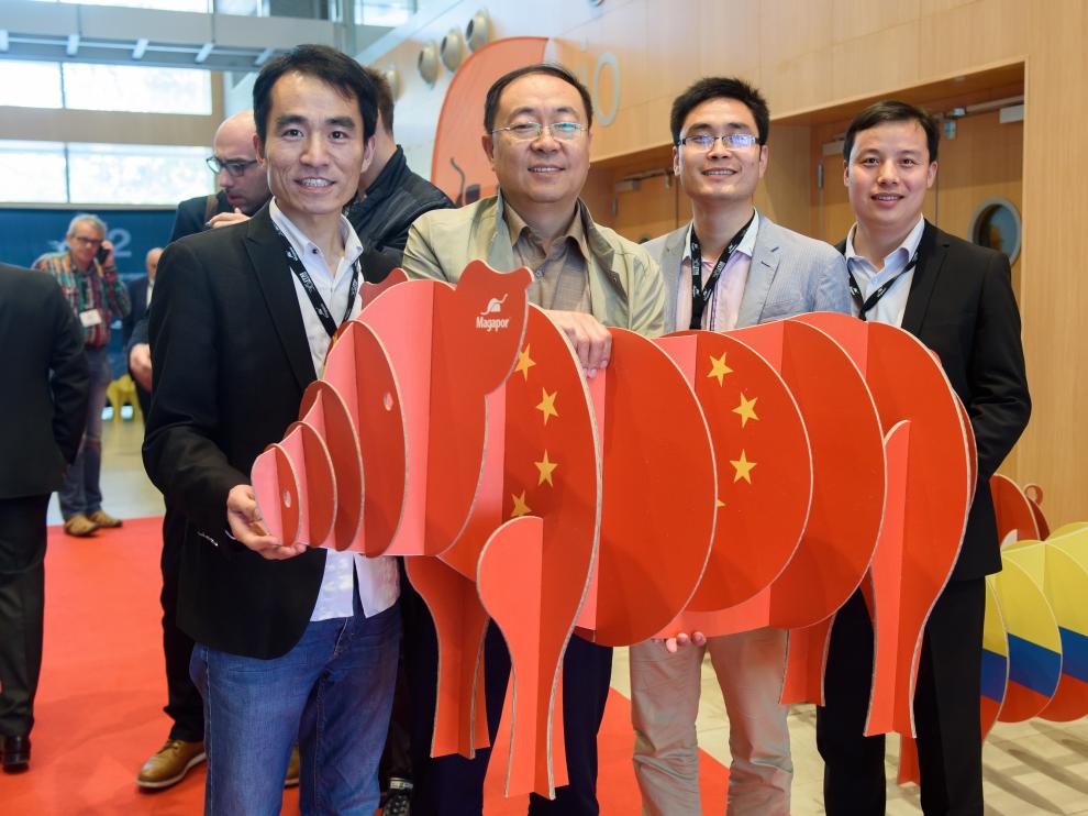 Imagen de cuatro clientes chinos que asistieron al último Encuentro Técnico Internacional que organiza Magapor anualmente en Zaragoza, sostienendo la figura de un cerdo elaborado por la entidad con la bandera su país.