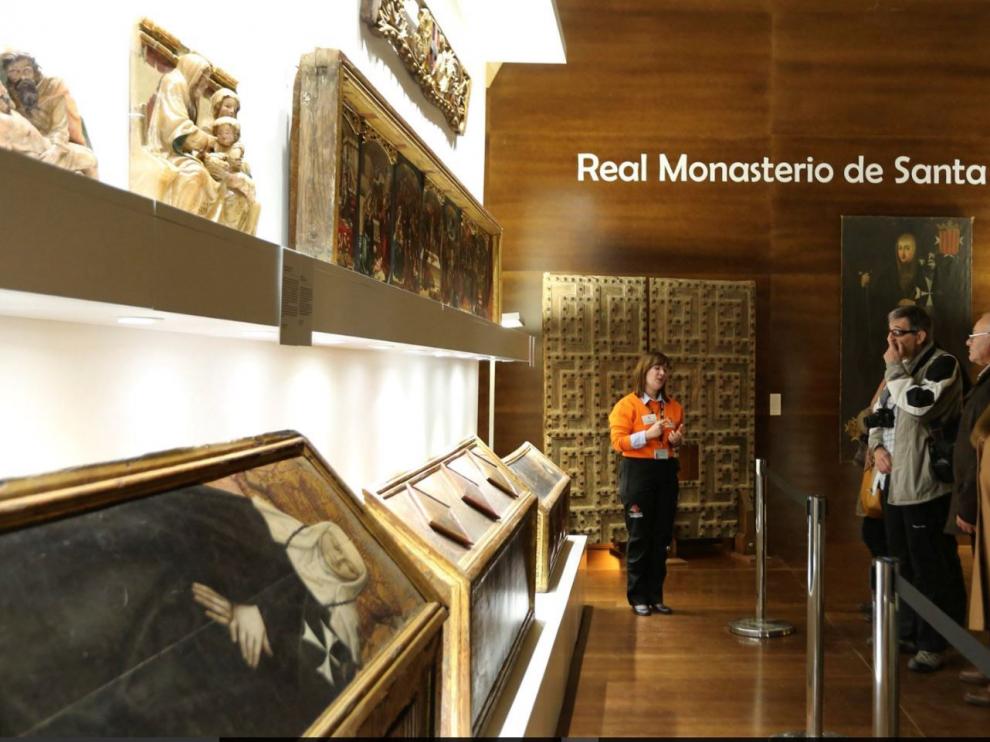 Un grupo de visitantes atiende a las explicaciones de la guía frente a las urnas funerarias y otros bienes de la colección de Sijena.
