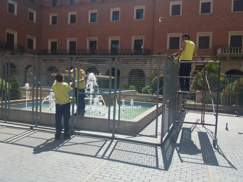 Unos operarios montan las vallas de protección de la fuente de la plaza de San Juan.