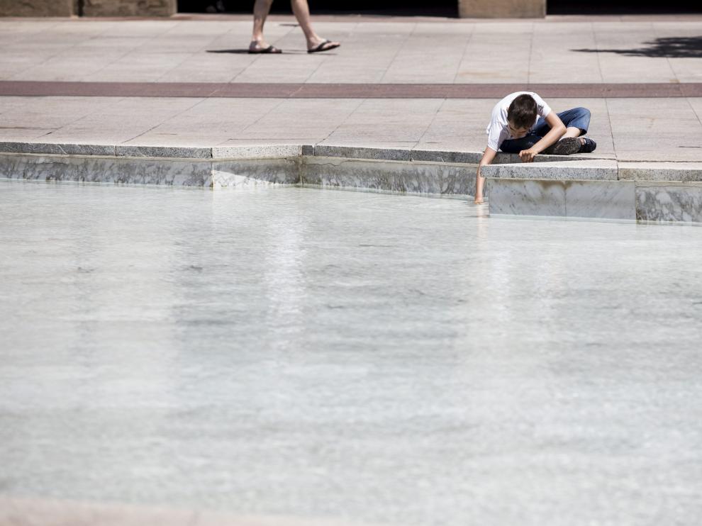 Un niño se refresca en una fuente en la plaza del Pilar.