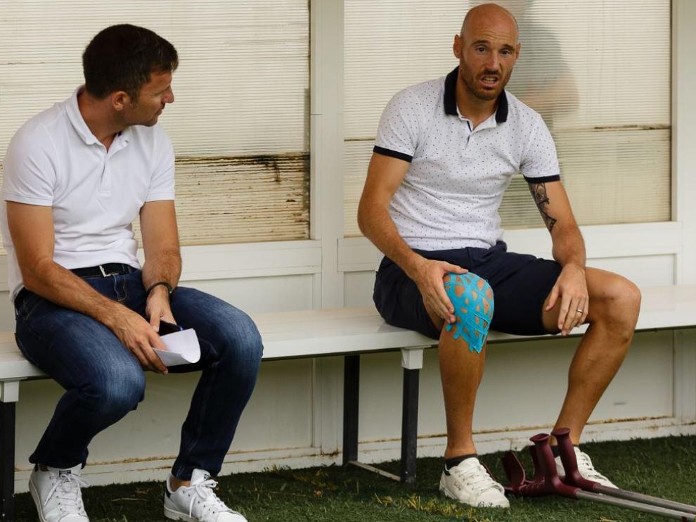 Toquero, con las muletas en el suelo y la rodilla dañada aún protegida, charla con el director deportivo Lalo Arantegui en el banquillo del campo del Tudelano, este sábado antes del partido amistoso del Real Zaragoza.