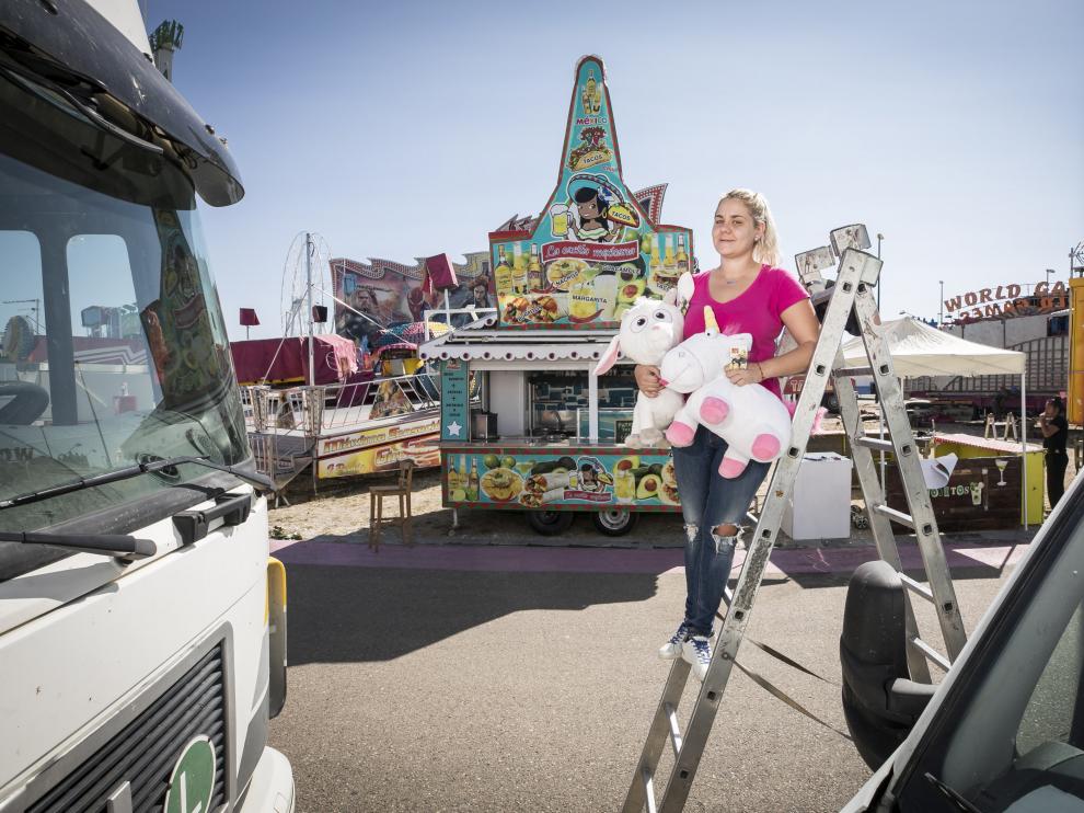 Icíar posa en la feria delante de su puesto de comida mexicana, subida a una escalera y agarrada a dos peluches, una cabra y un unicornio.