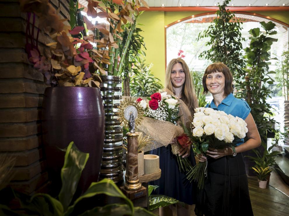 Teresa Villaverde (derecha) y Margarita Solano, posan con ramos de flores, junto a una imagen de la Virgen, en la floristería Los Sitios, en Zaragoza.