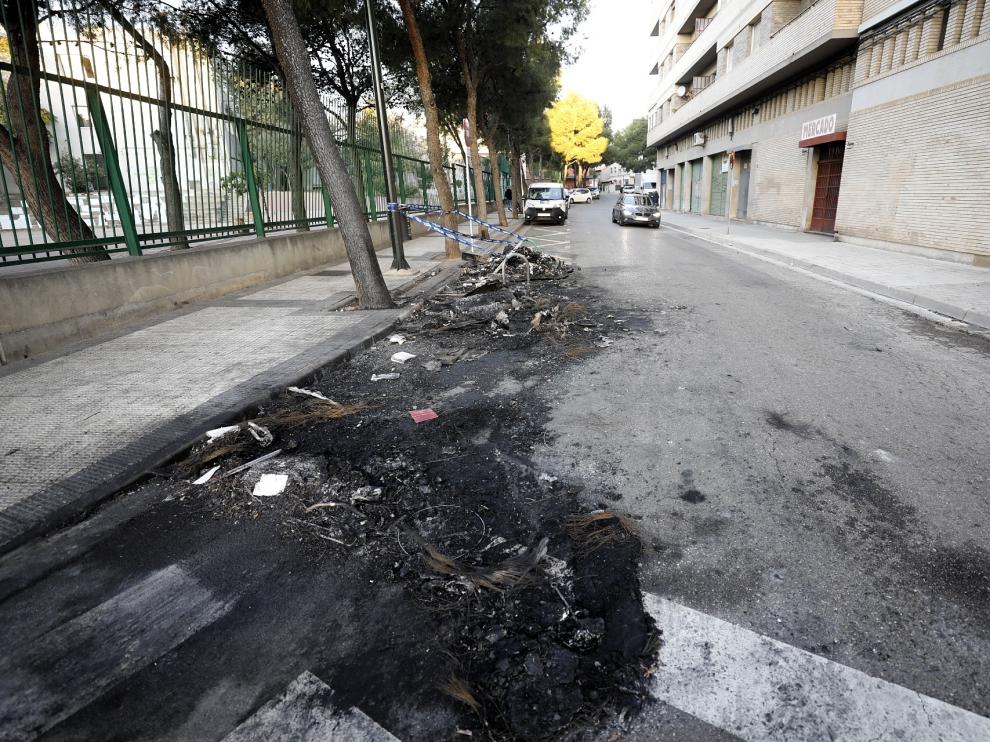 Restos del contenedor y el vehículo quemado en la calle de San Eugenio en Torrero.