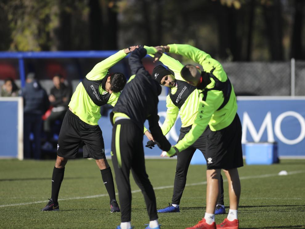 Cuatro jugadores de la SD Huesca realizan estiramientos en un entrenamiento.