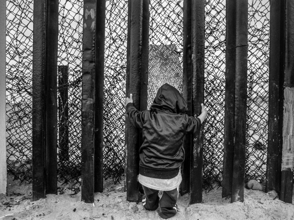 Un niño se agarra a los barrotes del muro fronterizo en la playa de Tijuana