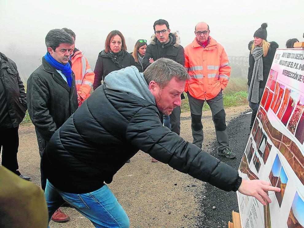 El consejero José Luis Soro señala una de la fotografías sobre la mejora de la carretera.