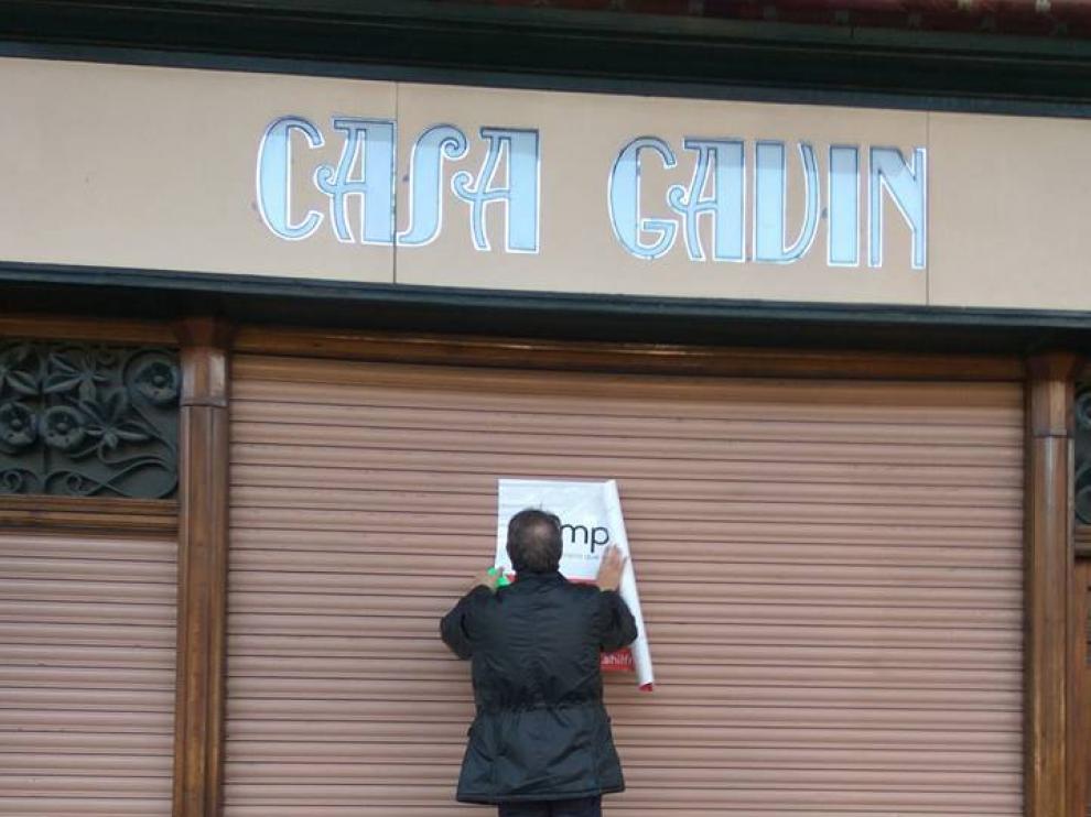 Un empleado de la inmobiliaria, colgando el cartel en el que se anuncia la venta del local de Casa Gavín.